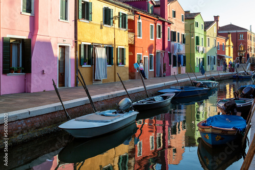 Burano, Venezia. Barche da pesca al palo in canale e case colorate con riflesso in acqua photo