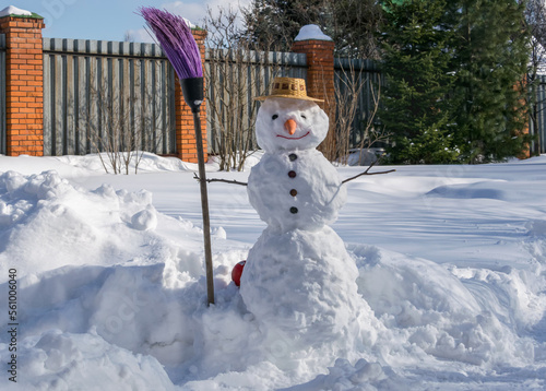  Snowman in a straw hat and a broom in his hand in a snowy garden.