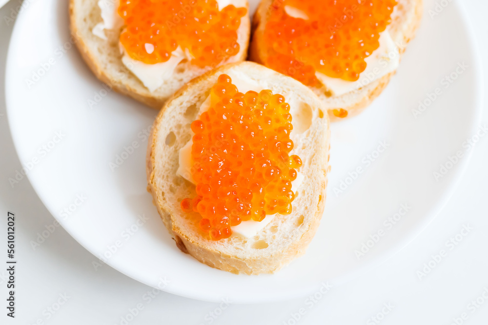 Slices of bread with red caviar on a plate, on a white background.
Slices of bread with red caviar on a plate, on a white background.
