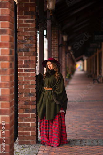 Elegant lady in vintage coat, red checkered dress and hat on Christmas background.Beautiful model in winter art pictures. Luxurly girl in holiday mood.