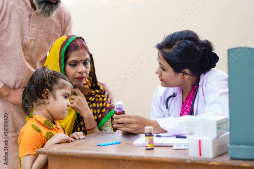 Photography Indian woman doctor giving liquid medicine to girl child at clinic