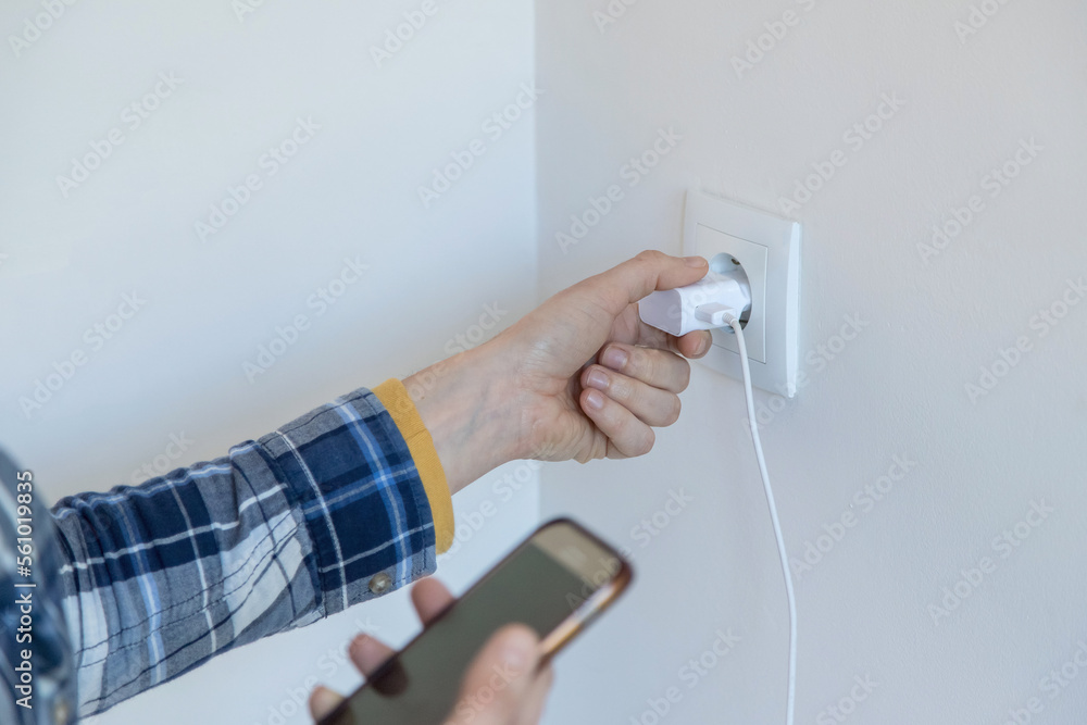 Closeup of a person holding a smartphone and a charger to put it on charge. Horizontal image and copy space. Closeup of a person holding a smartphone and a charger to put it on charge. Horizontal image and copy space.
