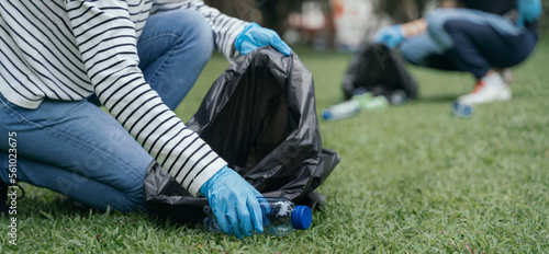 Women and men store plastic waste bottles in black bags at the park in the morning light.