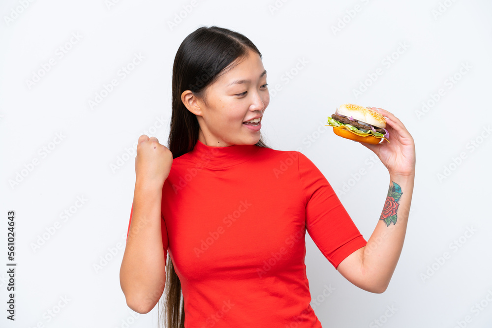 Young Asian woman holding a burger isolated on white background celebrating a victory Young Asian woman holding a burger isolated on white background celebrating a victory