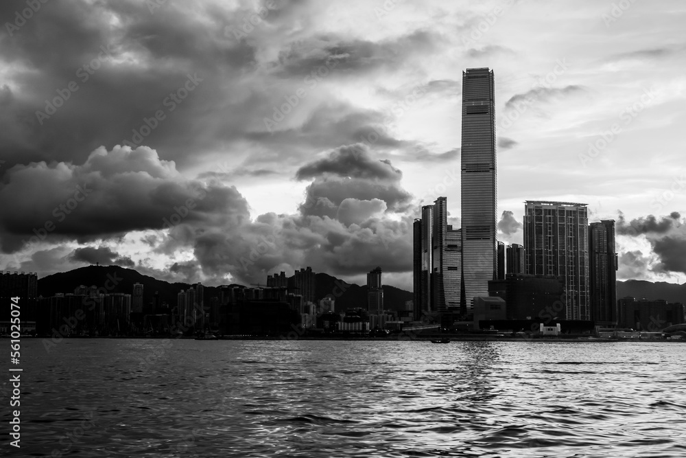 Early morning light.  The sun rises over Kowloon, Hong Kong.  Sea in the foreground.  Buildings in silhouette.  In black and white.