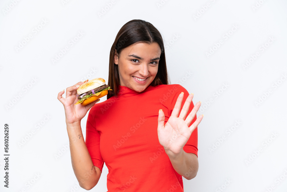 Young caucasian woman holding a burger isolated on white background saluting with hand with happy expression Young caucasian woman holding a burger isolated on white background saluting with hand with happy expression