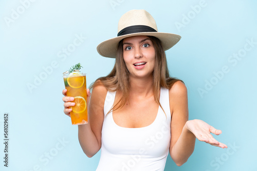 Young beautiful woman holding a cocktail isolated on blue background with shocked facial expression