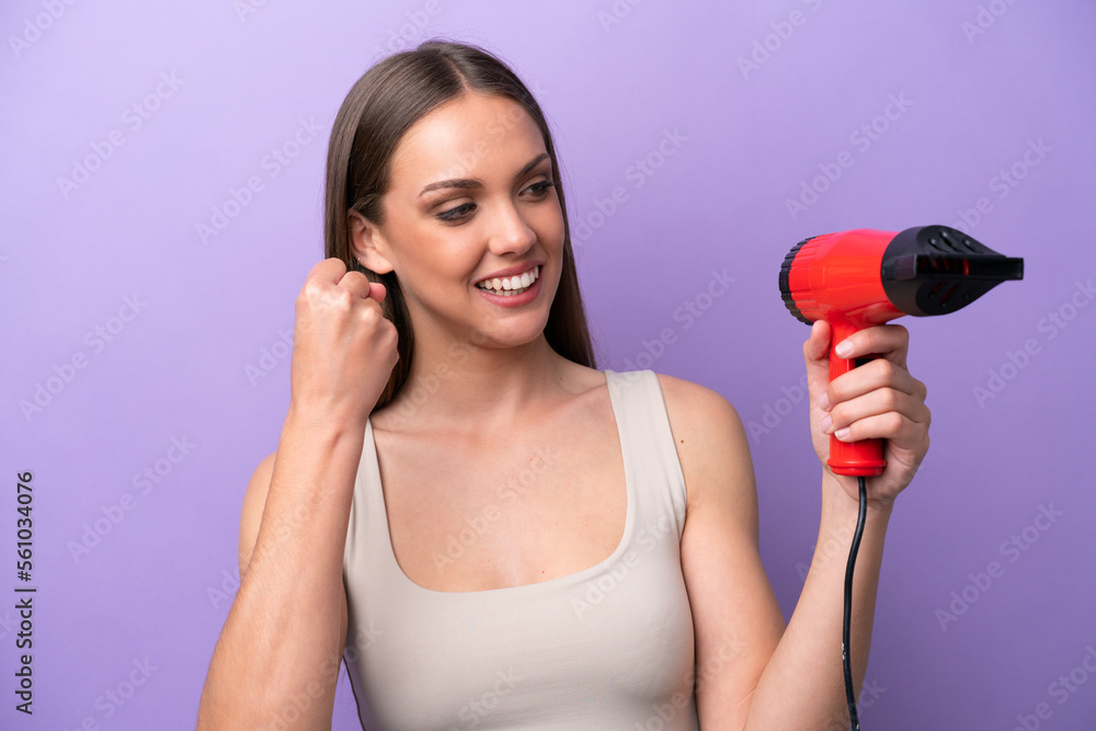 Young caucasian woman holding a hairdryer isolated on purple background celebrating a victory Young caucasian woman holding a hairdryer isolated on purple background celebrating a victory