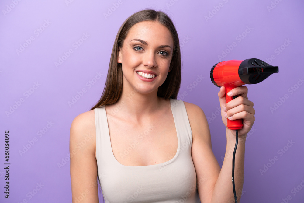 Young caucasian woman holding a hairdryer isolated on purple background with surprise and shocked facial expression Young caucasian woman holding a hairdryer isolated on purple background with surprise and shocked facial expression