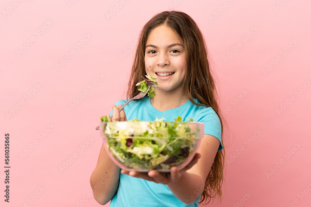 Little caucasian girl isolated on pink background holding a bowl of salad with happy expression