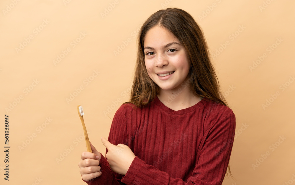 Little caucasian girl brushing her teeth isolated on beige background pointing back Little caucasian girl brushing her teeth isolated on beige background pointing back