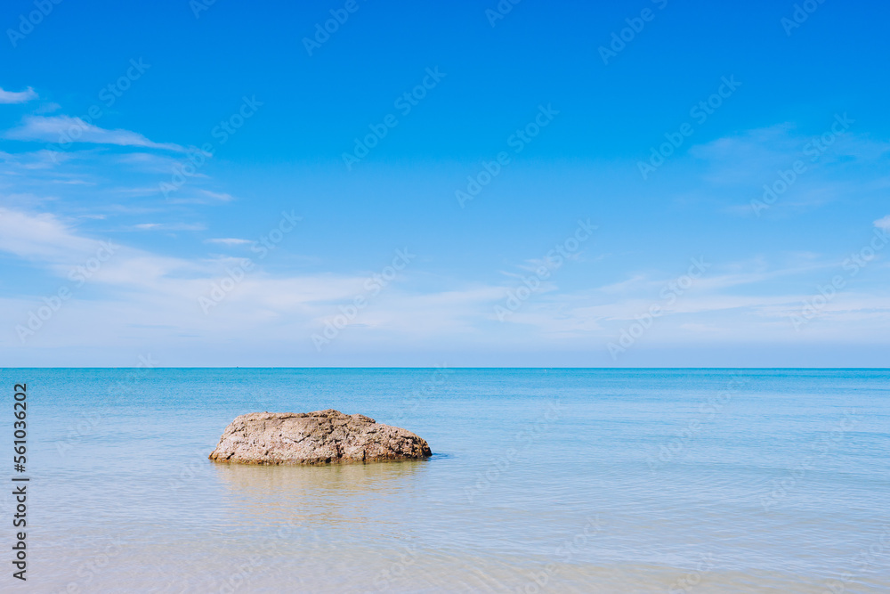 A lonely rock in the smooth sea or ocean with clear cloud and blue bright sky background at the sandy beach on summer time
