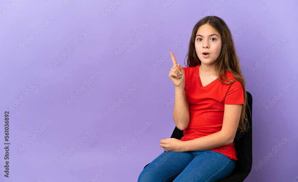 Little caucasian girl sitting on a chair isolated on purple background intending to realizes the solution while lifting a finger up Little caucasian girl sitting on a chair isolated on purple background intending to realizes the solution while lifting a finger up