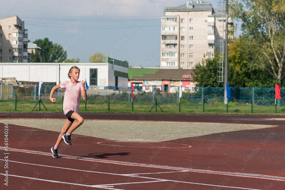 Fototapeta premium Young girl running on the running track at the stadium outdoors