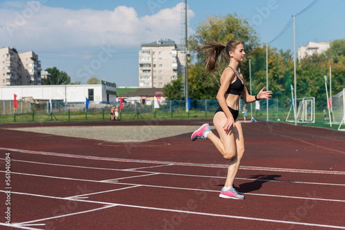 Young girl running on the running track at the stadium outdoors