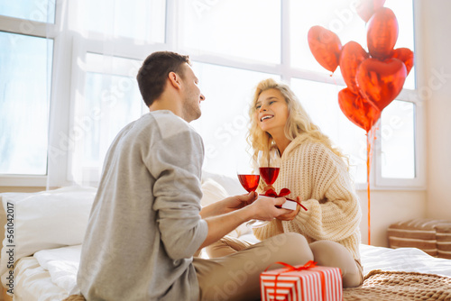 Young couple at home celebrating Valentine's Day  with glass of red wine. Romantic day together. Relationship, surprise and love concept.