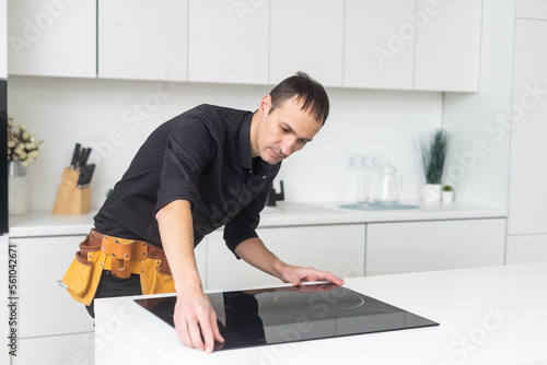 Man electrical repairs kitchen surface apartment. Installing hob in countertop. Man bought new kitchen furniture and appliances. Process installing an electrician household appliances.