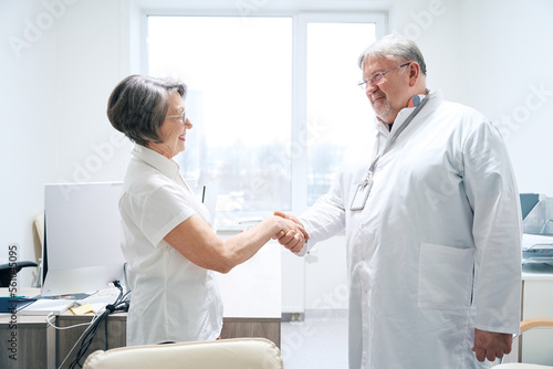 Friendly doctor greets with handshake elderly woman in medical office