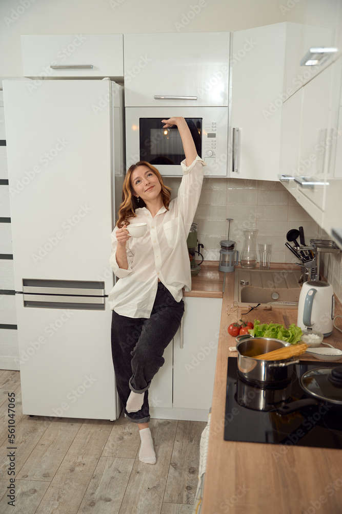Happy young housewife stretching with cup of coffee in hand Happy young housewife stretching with cup of coffee in hand