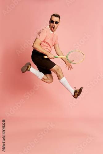 Portraits of handsome charismatic man in stylish clothes emotionally posing with tennis racket over pink studio background. Concept of fashion, sport, lifestyle photo