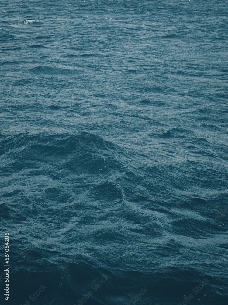 Vertical view of dark blue-green color of water surface with waves in middle of endless deep sea. Dark blue waves in deep ocean. Raging aquamarine waves on surface of the water.