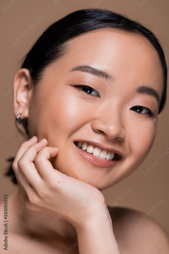 Portrait of cheerful asian woman with naked shoulder smiling at camera isolated on brown. Portrait of cheerful asian woman with naked shoulder smiling at camera isolated on brown.