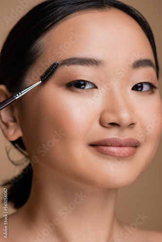 Portrait of young asian woman with makeup holding eyebrow brush isolated on brown.