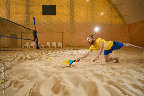 Man touches sand with a racket indoors during a game