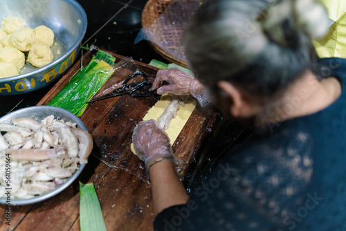 Making (wrapping) Tet Cake (Bánh Tét), the Vietnamese lunar new year Tet food outdoor with old woman hands and ingredients. Closed-up.