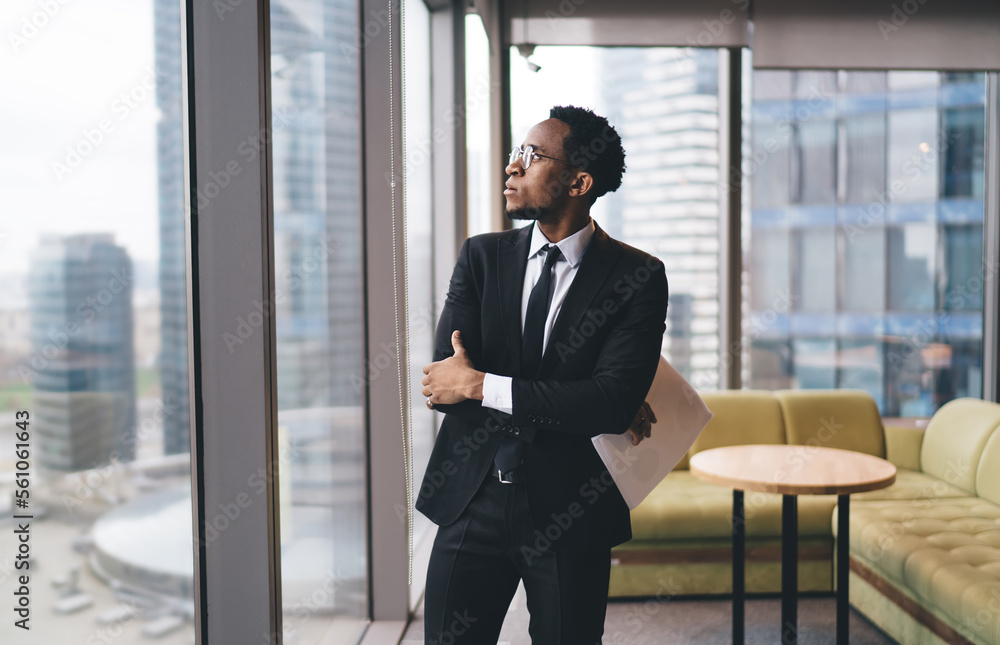 Pensive black businessman in suit standing near window Pensive black businessman in suit standing near window