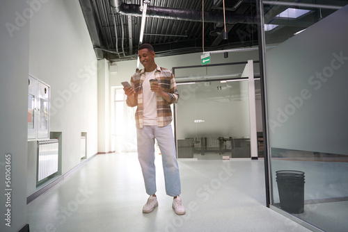 Happy young man using smartphone while standing in office hall