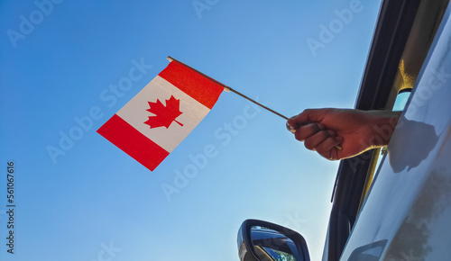 Boy waving Canada flag against the blue sky from the car window close-up shot. Man hand holding Canadian flag