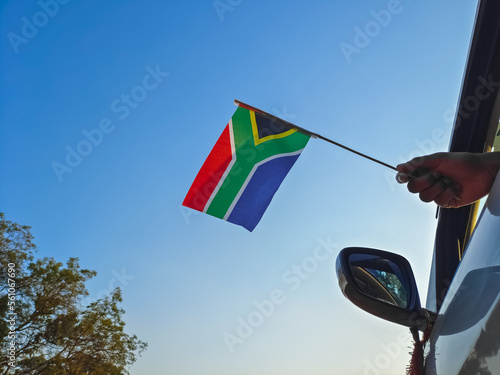 Boy waving South Africa flag against the blue sky from the car window close-up shot. Man hand holding South African flag