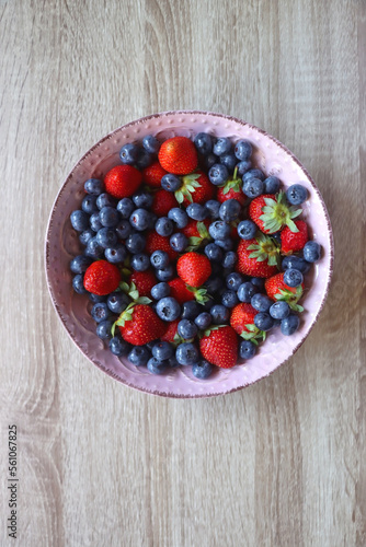Pink rustic bowl filled with fresh blueberries and strawberries. Wooden background  top view.