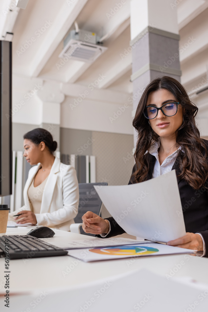businesswoman in eyeglasses working with documents near keyboard and multiracial colleague. businesswoman in eyeglasses working with documents near keyboard and multiracial colleague.