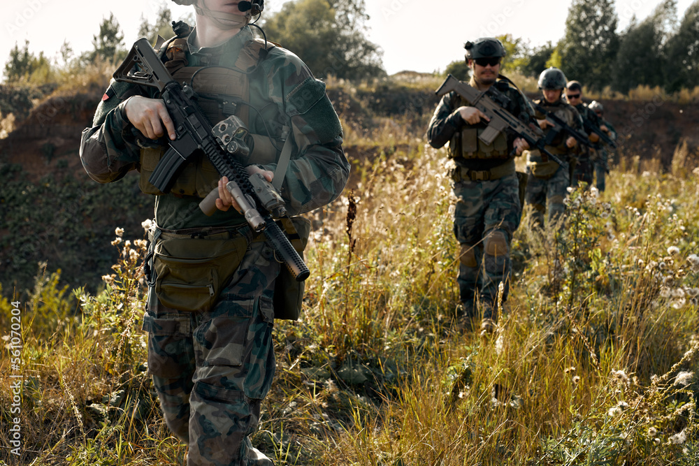 team of young and brave strong soldiers walking in countryside abandoned area, military training. young armed men in camouflaged uniform going in row. Infantry combat soldiers, military