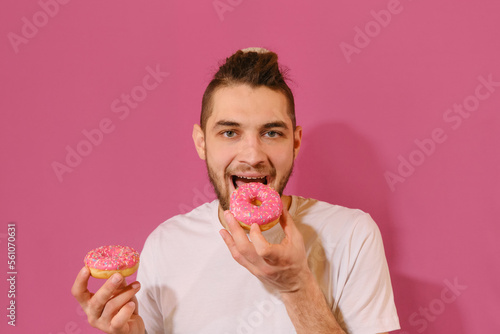 Concept of delicious but harmful food. Caucasian man with dreadlocks and unhealthy greasy food. Young handsome man holds pink glazed donuts in hands and wants to eat them.