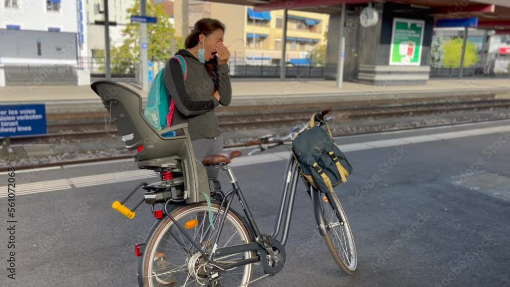 Tired woman yawning standing at platform waiting for train to arrive with bicycle. Person commuting in the morning Tired woman yawning standing at platform waiting for train to arrive with bicycle. Person commuting in the morning