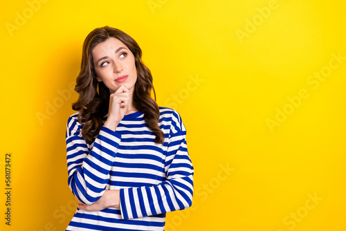 Photo portrait of pretty young girl look skeptical empty space consider dressed stylish striped outfit isolated on yellow color background