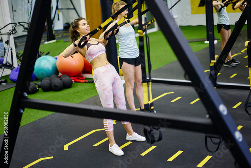 Fit sportswomen doing TRX exercise in gym