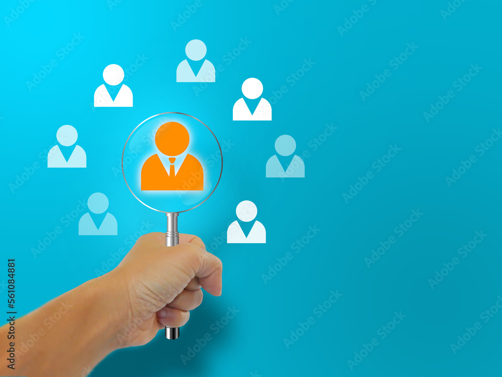 A hand holding a magnifying glass looking at a potential personnel icon, among many others. HMR or Human Resource Management. Human development and recruitment, leadership, and target group concept. A hand holding a magnifying glass looking at a potential personnel icon, among many others. HMR or Human Resource Management. Human development and recruitment, leadership, and target group concept.