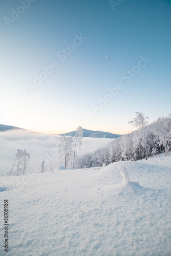 Morning idyll on the top of a snow-covered mountain with the rays of the sun irradiating the clouds, the ice cap of the mountain and a sliver of the moon. Beskydy mountains, Czech republic © Fauren
