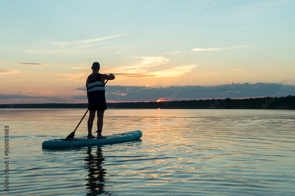 A man on a SUP board with a paddle at sunset against a purple sky floats in the water of the lake.