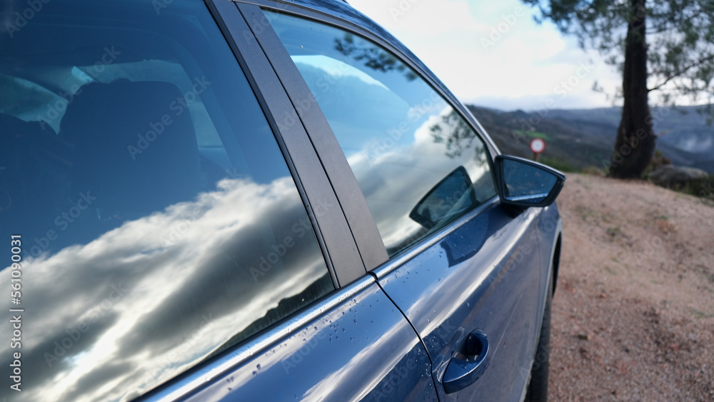 Naklejka premium Coche aparcado en la naturaleza con el reflejo de las nubes en el cristal