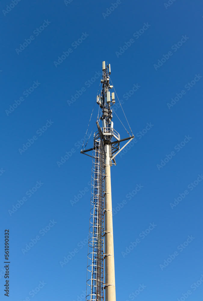 Communication tower with mobile cellular antennas against the blue sky on a sunny day. Tall pole with ladder