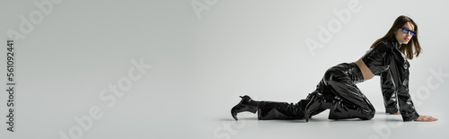 Photos full length of stylish young woman in black latex clothing and sunglasses posing on grey, banner