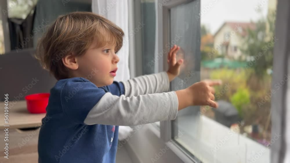 Child sitting by window home pointing outside. One small boy points finger stands by window Child sitting by window home pointing outside. One small boy points finger stands by window