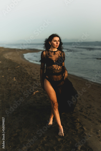 Portrait woman in sexy black dress walking with on the winter beach