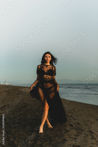 Portrait woman in sexy black dress walking with on the winter beach