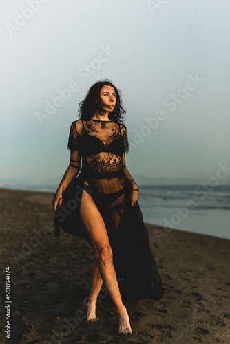 Portrait woman in sexy black dress walking with on the winter beach